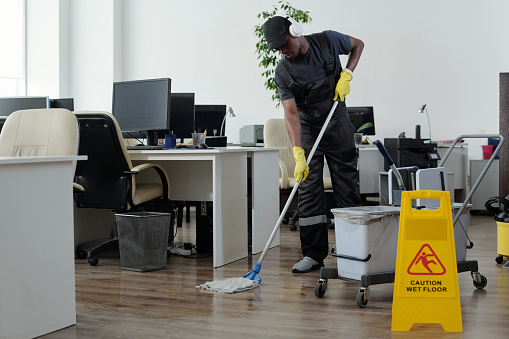 Contemporary young black man in workwear cleaning floor in openspace office