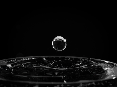 Closeup of a single water droplet hitting the surface, black and white