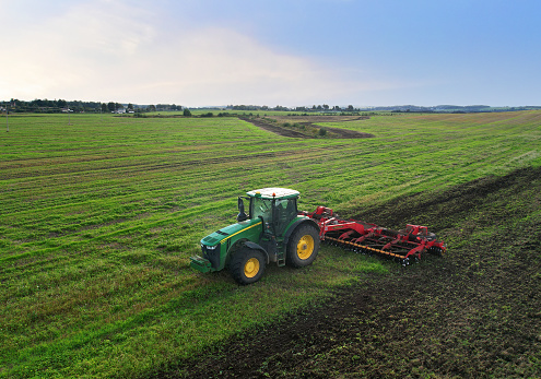 Plowing field. John Deere Tractor with disc cultivator Vaderstad on cultivating field. Agricultural tractor on cultivation field. Soil Tillage and sowing seeds. Russia, Smolensk, September 07, 2021.