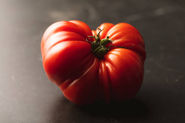 istock Fresh ripe tomato beefsteak on black background 1393772101