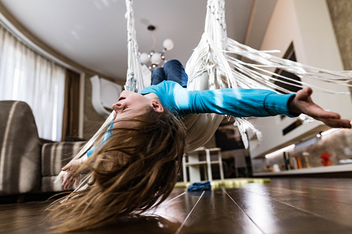 Carefree little boy having fun while swinging upside down with his arms outstretched in the living room.