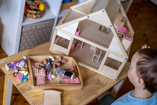 Montessori material. Toddler while playing with big pink dollhouse and having a great time. Gender confident little boy breaking stereotypes and socially imposed expectations.