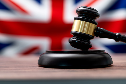 Law and justice concept,  gavel on a wooden desktop and the United Kingdom flag on background. 3d render.