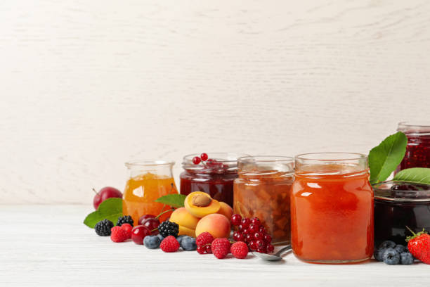 istock Jars with different jams and fresh fruits on white wooden table. Space for text 1393776879