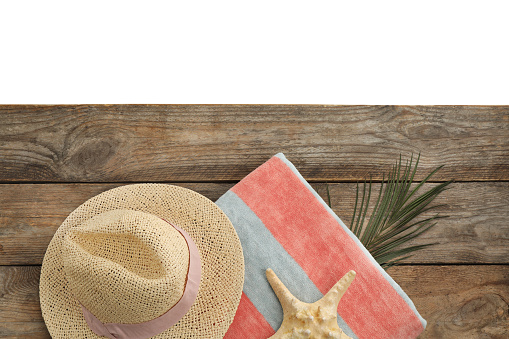 Wooden surface with beach towel and straw hat on white background, top view