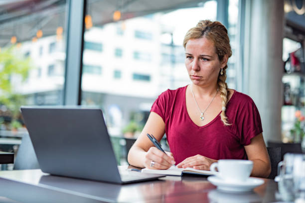 Woman using laptop and writting notes in coffee bar stock photo