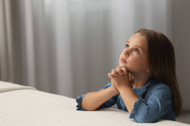 linda niña con las manos juntas diciendo oración antes de acostarse en el dormitorio. espacio para texto - christ child fotografías e imágenes de stock