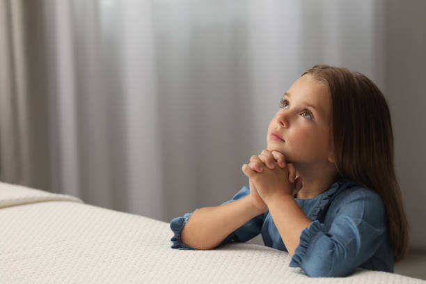 милая маленькая девочка со сцепленными руками читает молитву перед сном в спальне. место для текста - catholic girl стоковые фото и изображения