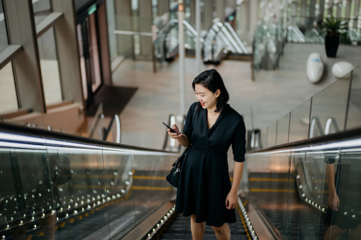 Young businesswoman using smartphone while riding on escalator