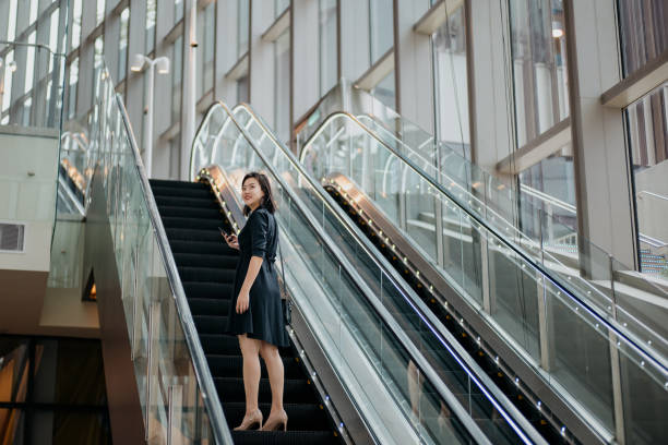 istock Young businesswoman using smartphone while riding on escalator 1393780206