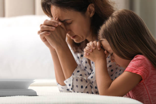 mature woman with her little granddaughter praying together over bible in bedroom - color image jesus christ child people imagens e fotografias de stock