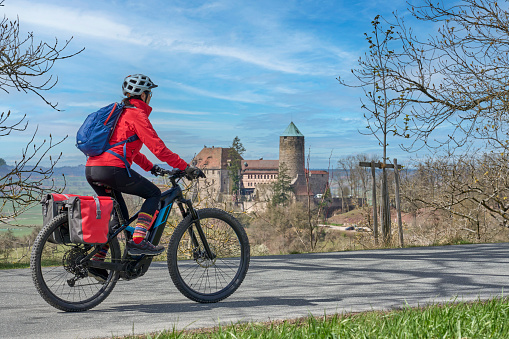 active senior woman on a cycling tour on the famous German route of castles, in front of the medieval castle of Colmberg, Franconia, Bavaria, Germany