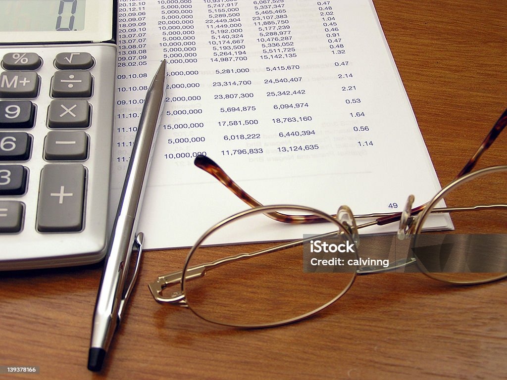 desk #2 stuff on top of a wooden desk - a piece of paper with numbers, pencil, calculator, and ladies' reading eyeglass. Focus on the numbers.<br> You may also like to consider  these: <br><a href='http://www.istockphoto.com/file_closeup.php?id=204716'><img src='http://www.istockphoto.com/file_thumbview_approve.php?size=1&id=204716' border='0'></a> <a href='http://www.istockphoto.com/file_closeup.php?id=205977'><img src='http://www.istockphoto.com/file_thumbview_approve.php?size=1&id=205977' border='0'></a> Calculator Stock Photo