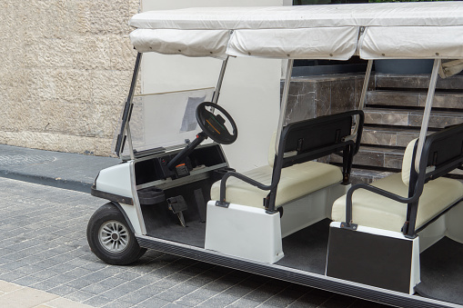 Golf car on the sidewalk. An empty tourist shuttle is parked outside the hotel. Electric golf cart