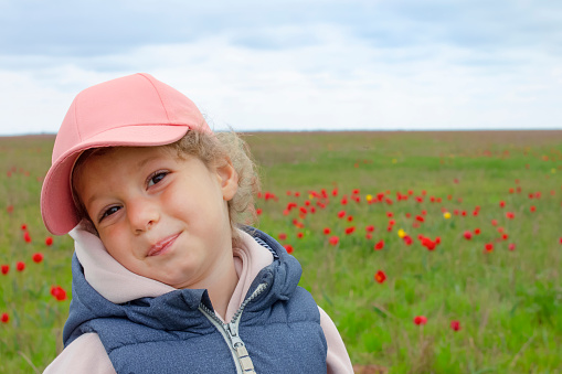 Cute little girl on the meadow in spring day. A child on a background of a green field with red flowers, tulips. Nature, fun, joy. Horizontal snapshot