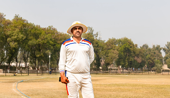 Portrait of smiling male cricket batsman wearing helmet standing on the field.