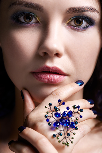 Portrait of beautiful brunette woman on black background. Female with blue eye shadow make up and manicure