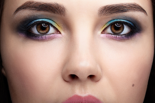 Closeup macro portrait of female face. Woman with evening beauty makeup. Girl with perfect skin and yellow - blue eye shadows