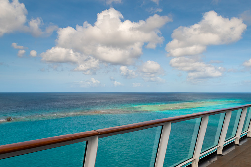 Beautiful and colorful image with railing of cruise ship, blue sky and white clouds, turquoise colored sea water at the port of Oranjestad in Aruba.