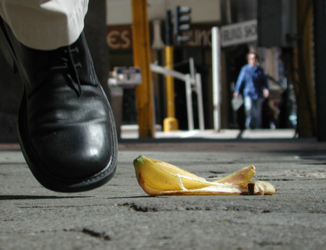 Man nearly steps on a banana peel on a city street.