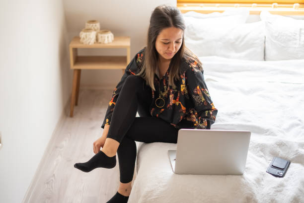 Young Woman wearing socks, using mobile devices in the morning Young Woman using mobile devices woman putting on socks stock pictures, royalty-free photos & images