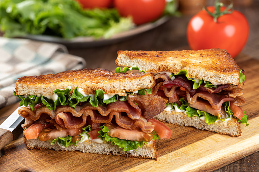 Blt sandwich made with bacon, lettuce and tomato on toasted whole grain bread cut in half on a wooden cutting board