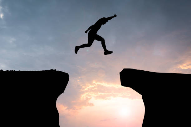 istock Silhouette young man jumping over precipice between two rocky mountains at sunset. 1393796285