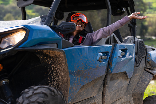 Excited extreme sportswoman driver enjoying and having fun while riding on an off-road vehicle. The woman wearing UTV Powersports goggles. An extreme, adrenaline-pumping adventure on the terrain, riding tour on a 4x4, Side-by-Side, UTV vehicle. Outdoor recreation activities. Off-Road Experience.