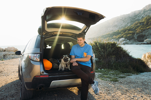 Happy male contemplating a road trip to the seacoast with a dog during sunset