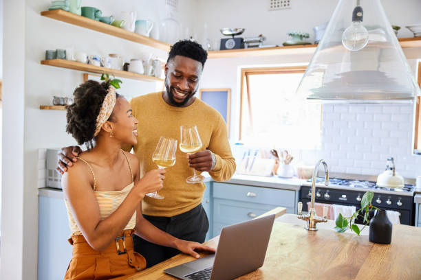 istock Smiling couple toasting with wine while using a laptop in their kitchen 1393799281