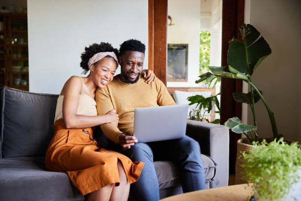 istock Smiling young couple using a laptop on their living room sofa 1393799401