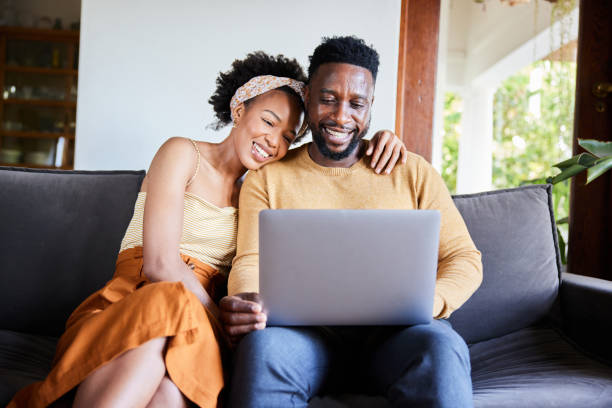 istock Young couple smiling while using a laptop on their living room sofa 1393799424