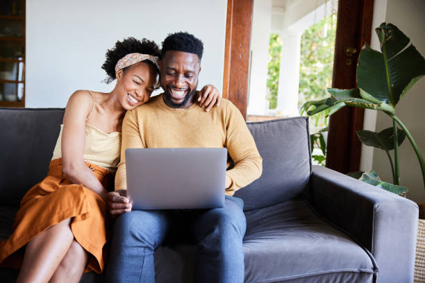 Laughing young couple using a laptop on their living room sofa stock photo