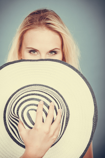 Summer fashion accessories concept. Shy blonde woman hiding behind summeral sun hat