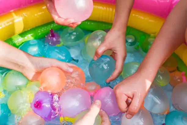 Photo of Water balloon games for kids. Close up of girls filling up water balloons at sunny day. Summer fun outdoor activities for children concept