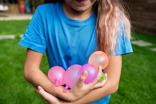 Water balloon games for kids. Smiling child girl holding colorful balls filled with water. Ready to fight! Summer fun outdoor activities for children concept