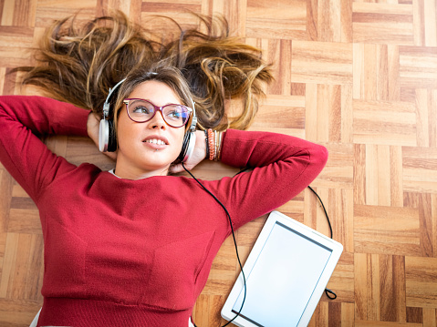 Young woman listening with headphones lying on the wooden floor