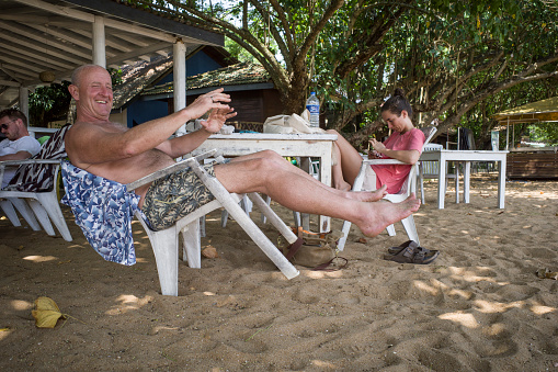 Unawatuna, Sri Lanka March 22, 2022 A tourist man leans and balances in a plastic chair on the beach.