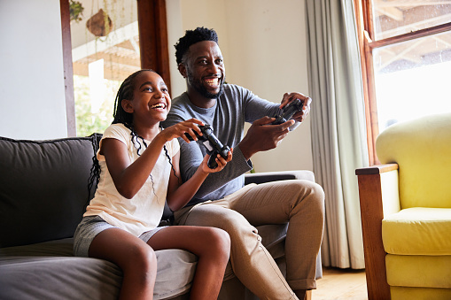 Laughing girl and her dad playing video games together at home