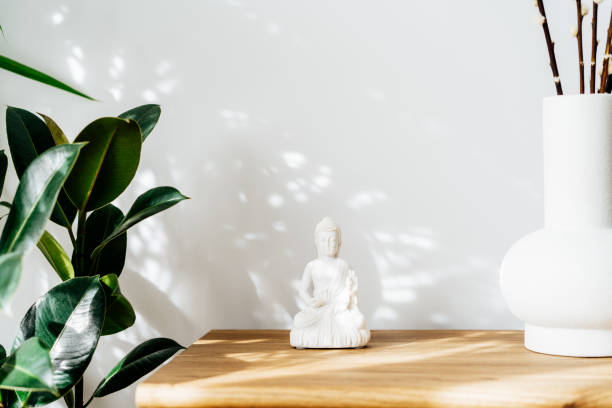 decoração de casa de estátua de buda branco e vaso de argila em pé no armário de madeira. design minimalista com plantas verdes e parede branca com sombras e destaques. decoração de design de interiores. foco seletivo. - sculpture contemporary buddha sparse - fotografias e filmes do acervo