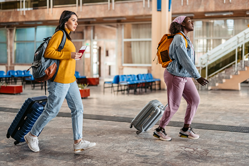 Two happy and excited young female tourists arriving for a train or a bus at the station. Holding passports.