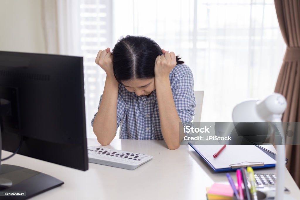 Stressed Asian woman sitting at working desk Medium shot of unrecognizable Asian woman sitting at desk, touching head, suffering from stress and overworked, having headache. Remote work or study at home and negative emotions concept. 30-39 Years Stock Photo