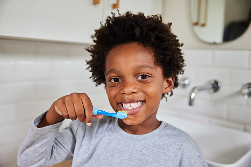 Close-up portrait of a cute little African boy brushing his teeth in her bathroom in the morning