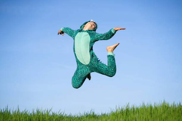 chłopiec w kostiumie dinozaura skacze szczęśliwy na niebie - arms raised green jumping hand raised zdjęcia i obrazy z banku zdjęć
