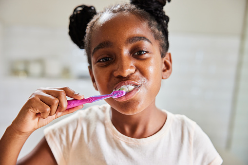 Close-up portrait of a cute little African girl brushing her teeth in her bathroom in the morning