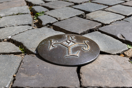 Aachen, Germany - Apr 18th 2022: Karolus Monogramm was the official symbol of Karl the Great. Symbols cast in bronze lead a route through Aachen old town.
