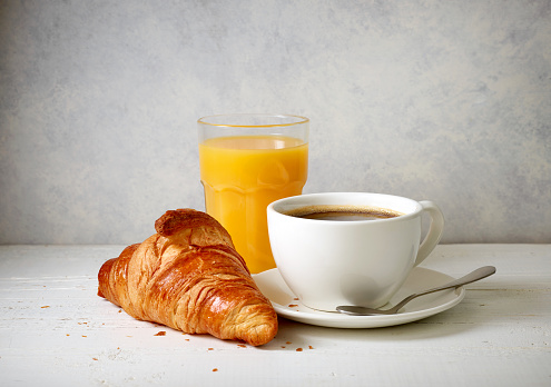 freshly baked croissant and cup of coffee on white wooden table