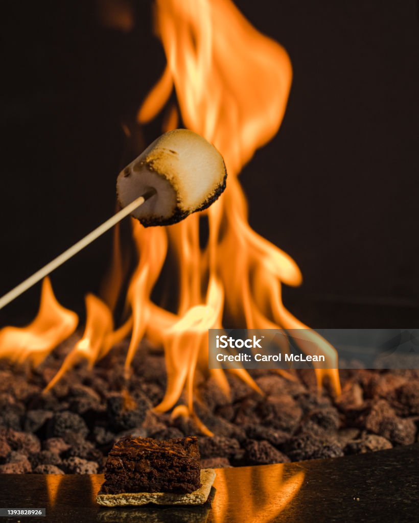 Toasting a marshmallow with a blurred fire in the background Smore Stock Photo