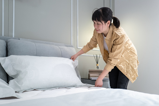 An Asian woman is making her bed at home