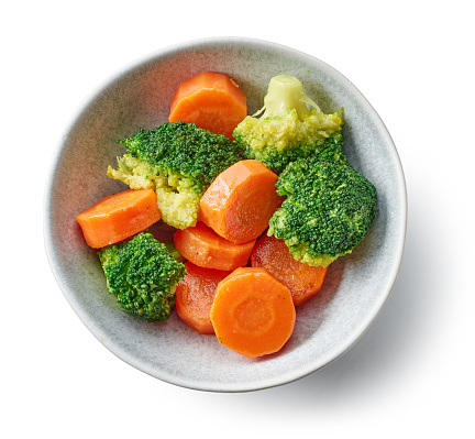 bowl of steamed and roasted carrots and broccoli isolated on white background, top view